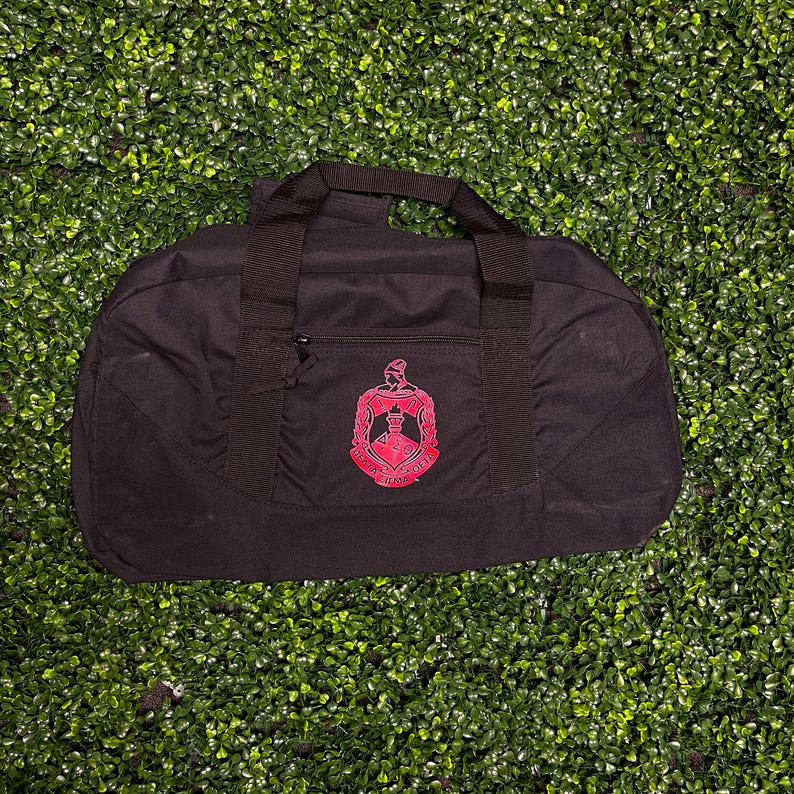 May include: Black duffel bag with a red embroidered Greek letter fraternity crest.