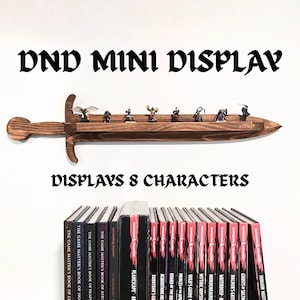 May include: A dark brown wooden wall shelf shaped like a sword, featuring a flat ledge for holding small figurines. The text DND MINI DISPLAY and DISPLAYS 8 CHARACTERS is printed above and below the shelf, which is mounted above several books.