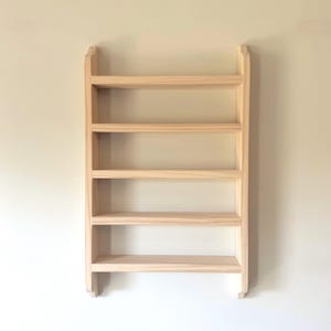 May include: A wall-mounted wooden shelf unit featuring five horizontal tiers for storage. The structure is crafted from light-colored, unfinished wood with a smooth grain, consisting of two vertical side panels and five evenly spaced shelves.