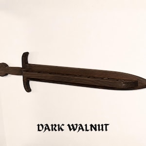 May include: A dark walnut wall-mounted display rack shaped like a sword. The wooden sword features a horizontal blade with a series of circular cutouts along the top edge for holding items. The text "DARK WALNUT" is printed below the object.