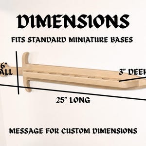 May include: A light-colored wooden sword-shaped display rack with circular cutouts for miniature bases. Text reads: DIMENSIONS, FITS STANDARD MINIATURE BASES, 6" TALL, 25" LONG, 3" DEEP, MESSAGE FOR CUSTOM DIMENSIONS. The rack is 25 inches long.