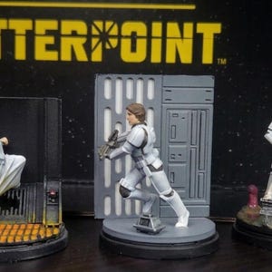 May include: Miniature figurines of Star Wars characters, including Princess Leia, a Stormtrooper, and Luke Skywalker. The figures are painted with detailed features and stand on themed bases. The word "SHATTERPOINT" is displayed in yellow text above.