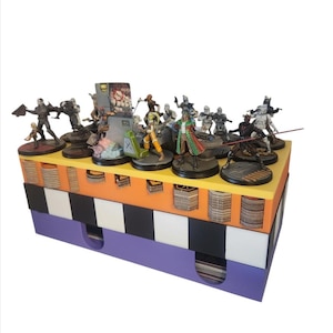 May include: A multi-level storage box with a purple base, black and white checkered middle section, and an orange top. The top level has a yellow border and holds miniature figures on circular bases. The figures are painted in various colors, including black, white, gray, brown, and green.