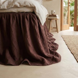 May include: A bed with a dark brown bed skirt and a light beige duvet cover. The bed skirt has a ruffled design and hangs to the floor. The bedding is made of a soft, textured fabric. The room has a neutral color palette.