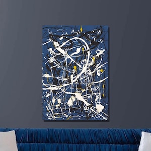 May include: Abstract art print featuring white, black, and yellow paint splatters on a dark blue background. The print is framed and hanging on a dark blue wall above a blue velvet sofa.