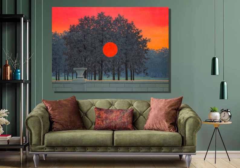 Op de afbeelding: Een groene fluwelen bank met twee kussens, een bruin en een met een rood, oranje en bruin patroon. Boven de bank hangt een schilderij van een rode zon die ondergaat achter een rij bomen.