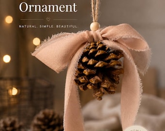 May include: A brown pinecone ornament hanging from a jute string with a light wooden bead and a frayed, dusty pink fabric bow. The text reads: HANDMADE Pinecone Ornament, NATURAL. SIMPLE. BEAUTIFUL., and a circular label says: HANDMADE with love.