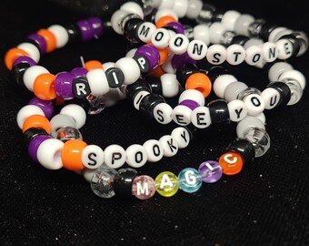 May include: Five colourful beaded bracelets with the words "RIP", "MOONSTONE", "I SEE YOU", "SPOOKY", and "MAGIC" spelled out in black letters.