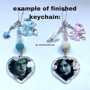 May include: Two heart-shaped keychains with images of people inside. Each keychain has a silver chain with a blue and pink butterfly charm, a pearl bead, and a smaller blue or pink butterfly charm.