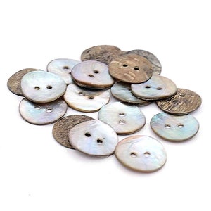 May include: A pile of 15 round, two-hole buttons made from natural coconut shell. The buttons are a light brown colour with a natural, slightly rough texture. Some of the buttons have a pearly iridescent sheen.