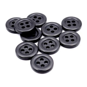 May include: A group of ten black, circular buttons, each with four holes. The buttons have a shiny finish and are arranged on a white surface. These buttons are ideal for various sewing and clothing projects.