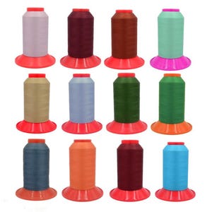 May include: Twelve colourful thread spools are displayed, including shades of pink, burgundy, brown, and green. Each spool is on a red and orange base, with a red top. These threads are suitable for sewing and crafting projects.