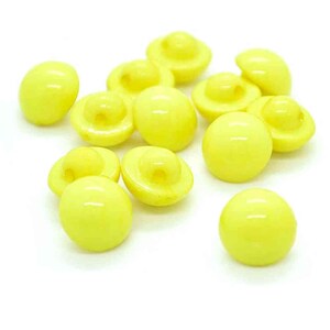 May include: A collection of 12 yellow plastic buttons. The buttons are round and have a raised centre.