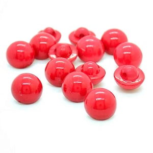 May include: A group of 12 bright red plastic buttons with a raised centre and a flat underside. The buttons are shiny and have a smooth finish.