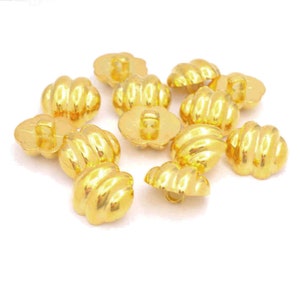 May include: A set of ten gold-coloured buttons with a ribbed design. The buttons are oval-shaped and have a hole in the centre for sewing.