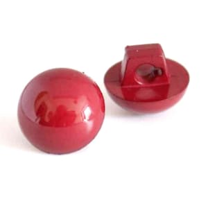 May include: Two red plastic buttons with a shank on the back. The buttons are round and have a glossy finish.