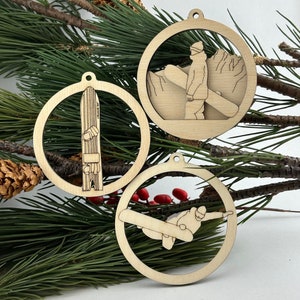 Three round wooden ornaments, one featuring a vintage split tail snowboard, one is a snowboarder performing a trick in the air and one is a snowboarder standing with snowboard in hand looking at distant mountains.