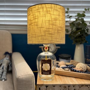 May include: A lamp made from a clear glass bottle with a brown label that reads 