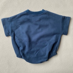 May include: A navy blue baby romper with short sleeves and a round neckline. The romper has a relaxed fit with a gathered waist and is made of a soft, comfortable fabric. The garment is designed for infants and toddlers.