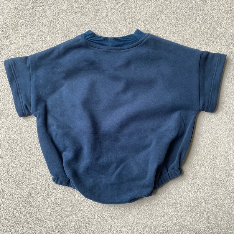 May include: A navy blue baby romper with short sleeves and a round neckline. The romper has a relaxed fit with a gathered waist and is made of a soft, comfortable fabric. The garment is designed for infants and toddlers.