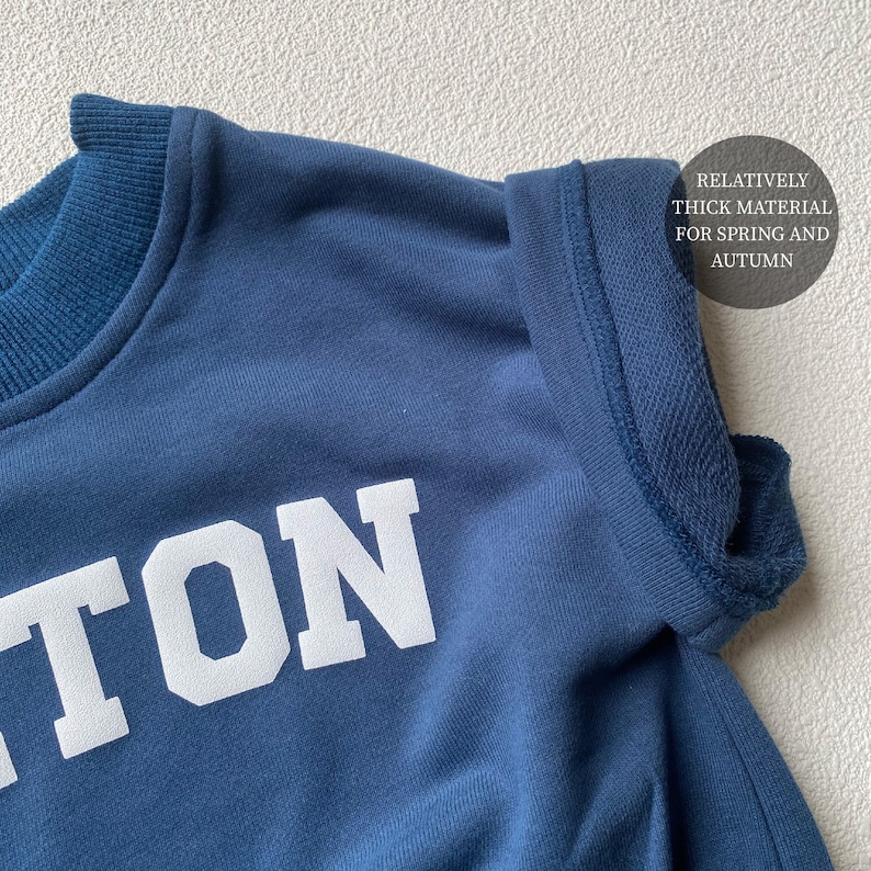 May include: Close-up of a navy blue sweatshirt with white block lettering. The sweatshirt has a crew neck and a thick material, suitable for spring and autumn wear. The text on the sweatshirt is partially visible.