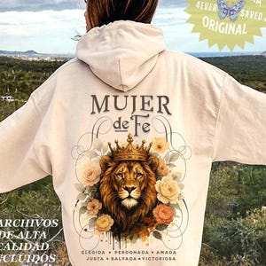 May include: Cream-colored hoodie with the Spanish text "MUJER de Fe" and a lion wearing a crown, surrounded by flowers. The hoodie also features the text "4 ARCHIVOS DE ALTA CALIDAD INCLUIDOS" and "ELEGIDA • PERDONADA • AMADA JUSTA • SALVADA • VICTORIOSA".