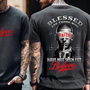 May include: Dark gray t-shirt with the word "Believe" in red script on the front. The back of the shirt features a graphic of a person with a blindfold that says "Faith" and the words "Blessed are those who have not seen yet Believe."
