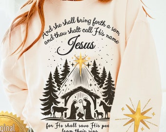 May include: Cream-coloured sweatshirt featuring a nativity scene graphic, a star, and the text "And she shall bring forth a son, and thou shalt call His name Jesus." The sleeve has a gold star design.