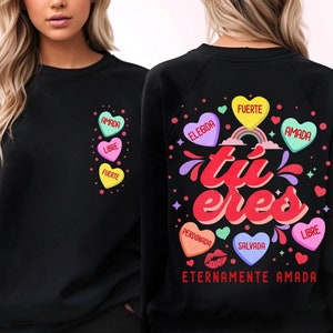 May include: Black sweatshirt with a rainbow and the text "tu eres" in red and white. The sweatshirt has several hearts with Spanish words on them, including "amada", "libre", "fuerte", "elegida", "perdonada", "salvada", and "eternamente amada".