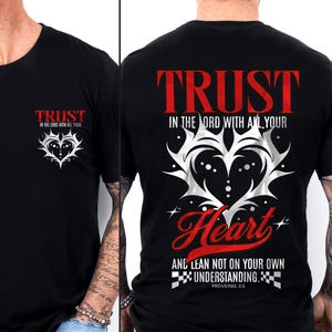 May include: Black t-shirt with the word "TRUST" in red on the front and back. The front features a heart design with text, while the back has a larger heart design and the phrase "IN THE LORD WITH ALL YOUR HEART".