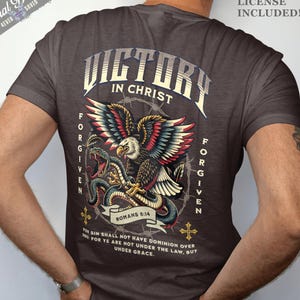 Könnte beinhalten: Dunkelgraues T-Shirt mit detaillierter Grafik eines Adlers und einer Schlange, mit den Worten "VICTORY IN CHRIST" und "FORGIVEN". Enthält den Text "ROMANS 6:14" und ein Zitat. Gewerbliche Lizenz enthalten.
