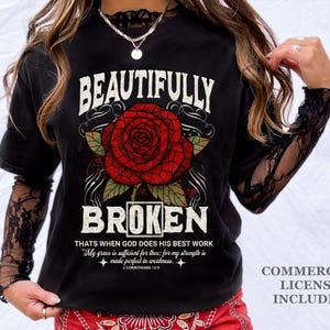 May include: Black t-shirt with a large red rose graphic and the words "BEAUTIFULLY BROKEN". The shirt also features a quote from 2 Corinthians 12:9. The shirt has long sleeves with a lace design.