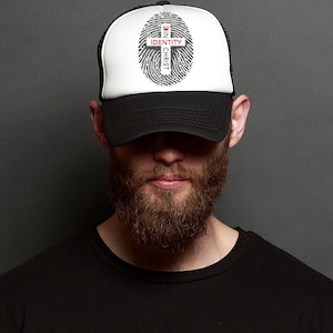 May include: A black and white trucker hat with a white mesh back. The front of the hat features a black and white fingerprint with a red cross and the text "IN CHRIST IDENTITY".