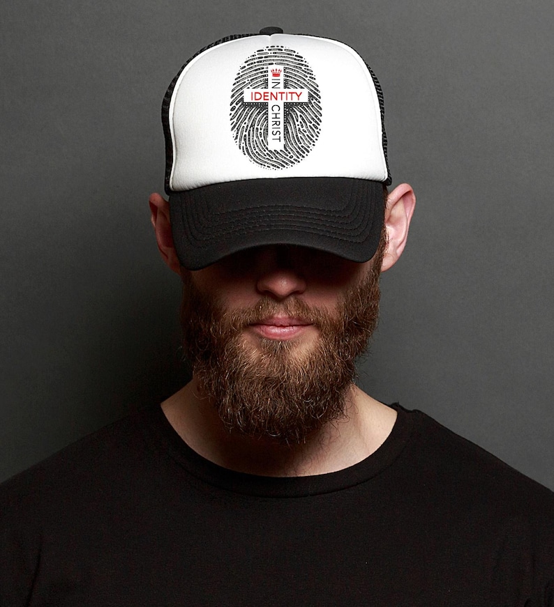 May include: A black and white trucker hat with a white mesh back. The front of the hat features a black and white fingerprint with a red cross and the text "IN CHRIST IDENTITY".