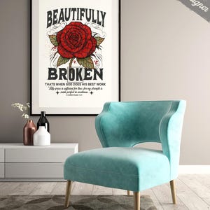 May include: A framed art print with the words "BEAUTIFULLY BROKEN" and a red rose illustration. Below the rose is the text "THATS WHEN GOD DOES HIS BEST WORK". A teal armchair with wooden legs sits in front of the print. The image also includes a white cabinet and decorative vases.