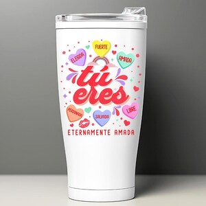 May include: White stainless steel tumbler with a colorful design featuring the words "tu eres" and hearts with Spanish words like "amada", "fuerte", and "salvada". The tumbler has a lid and a handle.