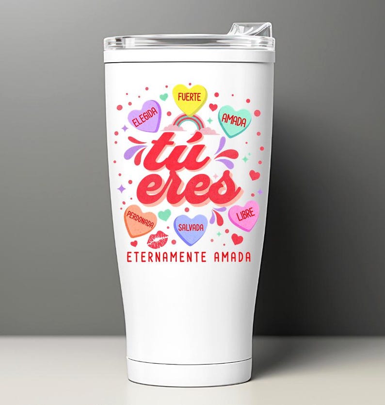 May include: White stainless steel tumbler with a colorful design featuring the words "tu eres" and hearts with Spanish words like "amada", "fuerte", and "salvada". The tumbler has a lid and a handle.