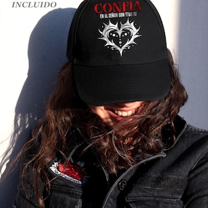 May include: Black baseball cap with the word "CONFIA" in red, and the phrase "EN EL SE&Ntilde;OR CON TODO TU" in white. The cap features a white heart design. The image also shows a black denim jacket.