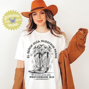 May include: White t-shirt with a graphic of cowboy boots filled with flowers, and the text "EL SE&Ntilde;OR GU&Iacute;A NUESTROS PASOS" and "PROVERBIOS 16:9". The shirt is worn with an orange hat and jacket. A logo that says "DISENADORA 4EVER SAVED ORIGINAL" is in the upper left corner.