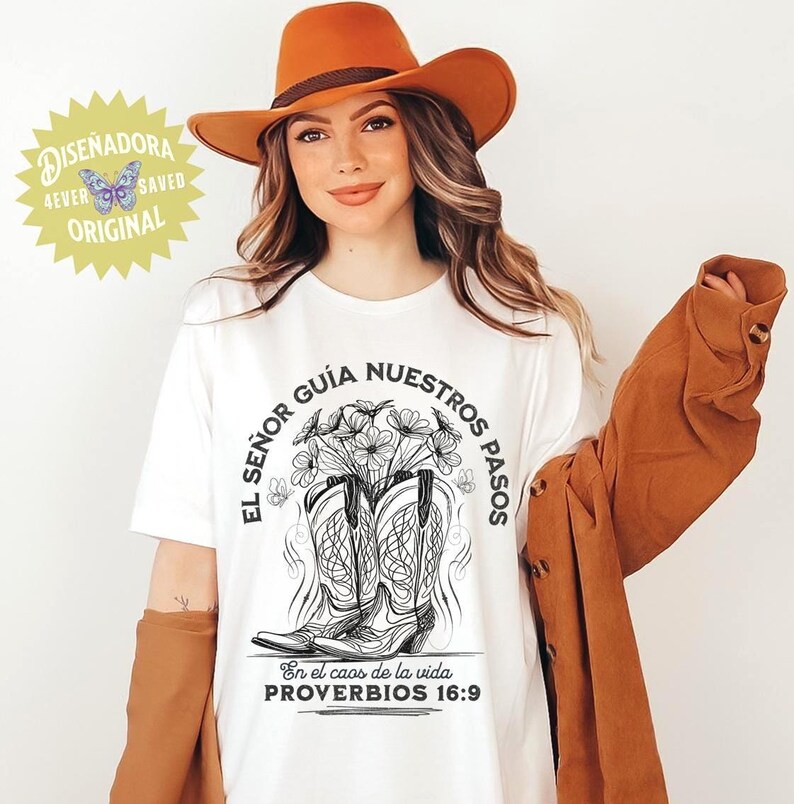 May include: White t-shirt with a graphic of cowboy boots filled with flowers, and the text "EL SE&Ntilde;OR GU&Iacute;A NUESTROS PASOS" and "PROVERBIOS 16:9". The shirt is worn with an orange hat and jacket. A logo that says "DISENADORA 4EVER SAVED ORIGINAL" is in the upper left corner.