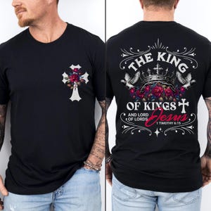 May include: Black t-shirt with a white cross and red roses on the left side. The back of the shirt has a white graphic with the text "The King of Kings and Lord of Lords Jesus 1 Timothy 6:15".