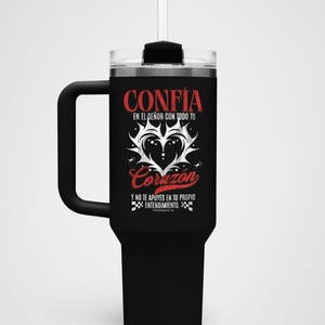 May include: Black insulated tumbler with a handle and a clear lid. The tumbler features the Spanish words "CONFIA" and "Corazon" in red script, along with other text and a heart design. Includes a straw.