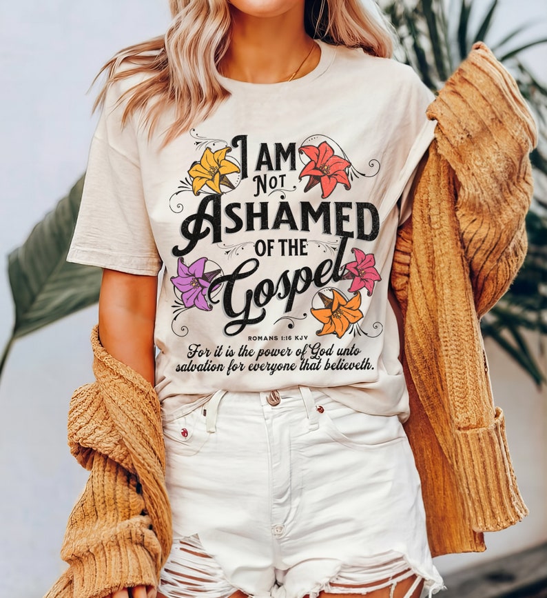 May include: A white t-shirt with a floral design and the text "I am not ashamed of the Gospel" with the scripture reference "Romans 1:16 KJV" and the text "For it is the power of God unto salvation for everyone that believeth."