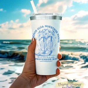 May include: White tumbler with a silver lid and a straw. The tumbler features a blue design of cowboy boots, flowers, and text in Spanish. The text reads "SE&Ntilde;OR GU&Iacute;A NUESTROS PASOS" and "En el caos de la vida PROVERBIOS 16:9".