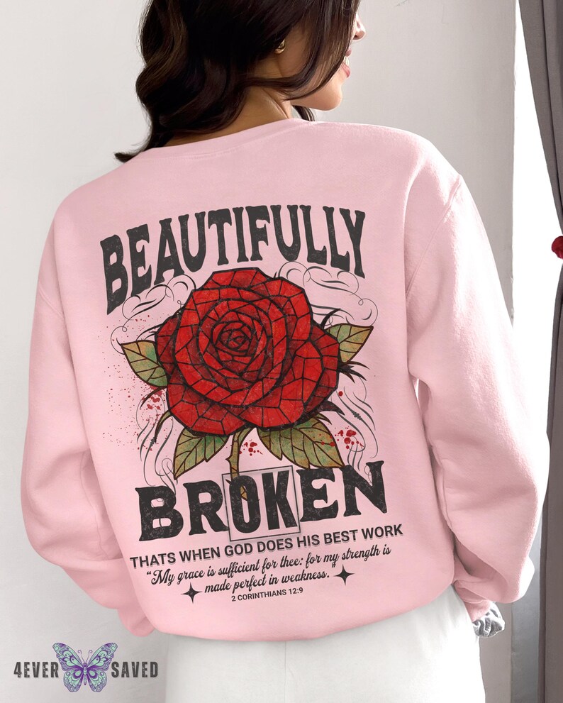 May include: Light pink sweatshirt with a large red rose graphic and the words "BEAUTIFULLY BROKEN". The text "THATS WHEN GOD DOES HIS BEST WORK" and a Bible verse are also printed on the back. The brand logo is at the bottom.
