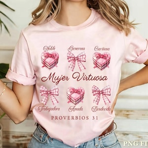 May include: Pink t-shirt with a watercolor design of hearts and bows. The text "Mujer Virtuosa" is written in red. The words "Noble, Generosa, Cari&ntilde;osa, Trabajadora, Amada, Bendicida" are written around the hearts. The text "Proverbios 31" is written at the bottom of the design.
