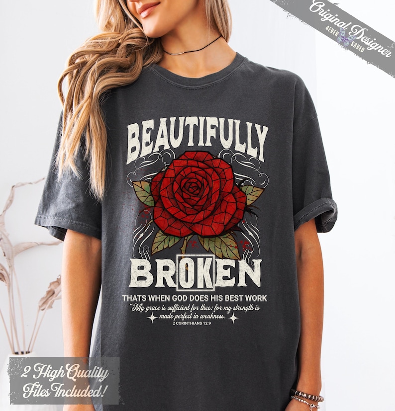 May include: Dark gray t-shirt with the words "BEAUTIFULLY BROKEN" above a red rose graphic. The shirt also features text from 2 Corinthians 12:9. The design includes the text "Original Designer" and "2 High Quality Files Included!"