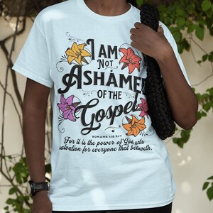 May include: Light blue t-shirt with a floral design and the text "I am not ashamed of the Gospel" with a Bible verse from Romans 1:16 KJV.