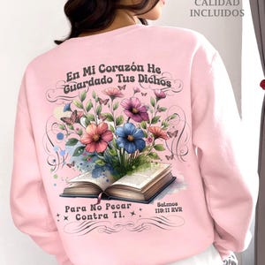 May include: Pink sweatshirt with a floral design and a book with the text "En Mi Corazón He Guardado Tus Dichos Para No Pecar Contra Ti. Salmos 119:11 RVR"