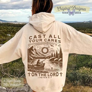 May include: Cream-colored hoodie with a graphic on the back featuring a lake scene with a person fishing, mountains, and the text "CAST ALL YOUR CARES ON THE LORD". The hoodie also has the text "Original Designer 4ever Saved".